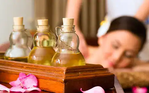Small glass bottles with essential oils on a wooden tray at a wellness or massage spa.